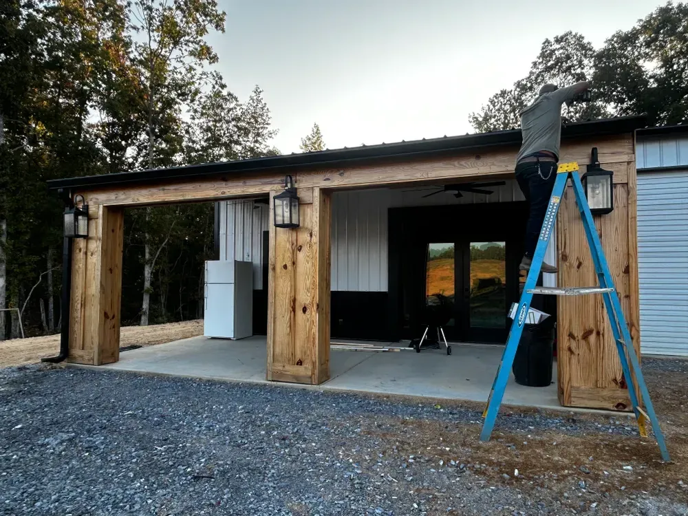 Man on ladder working on the exterior of a building with a metal roof and wooden beams.