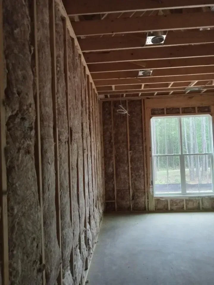 Interior view of a building under construction. Studs and insulation are visible in the walls, and a window is in place.