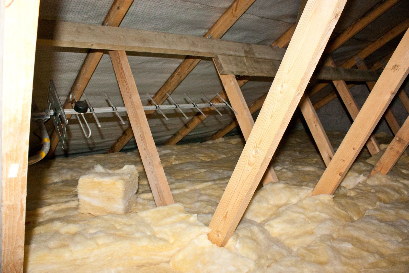 Inside a house attic: wooden rafters, insulation, and a silver antenna.