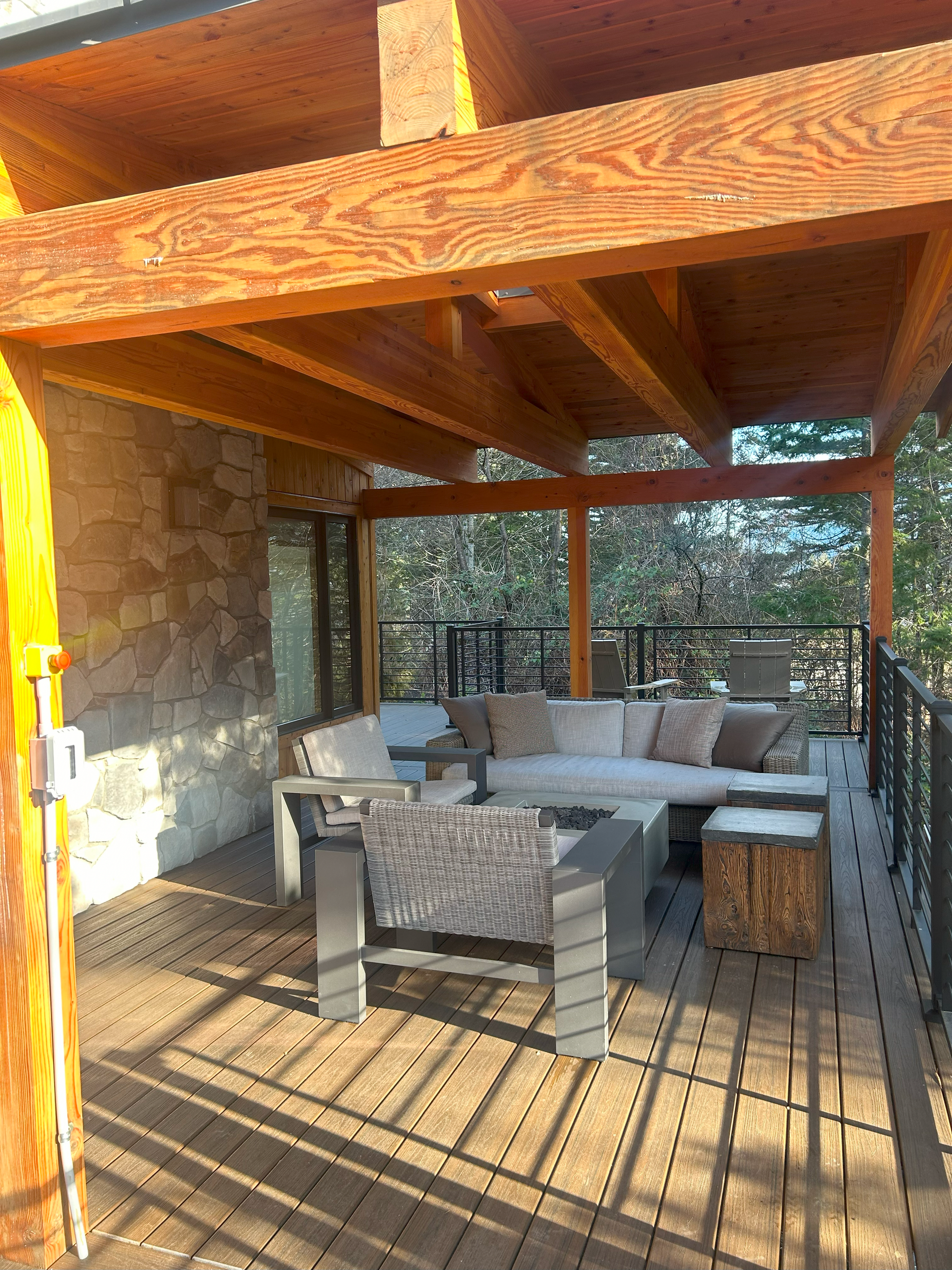 A wooden deck with a couch and chairs under a wooden pergola.