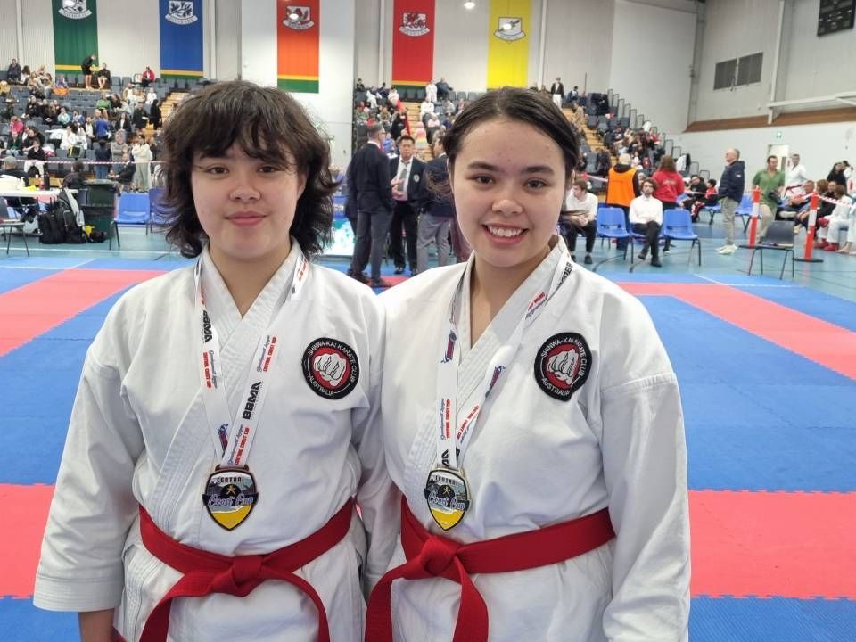 Martial arts students in white uniforms pose in a studio with raised arms and red belts