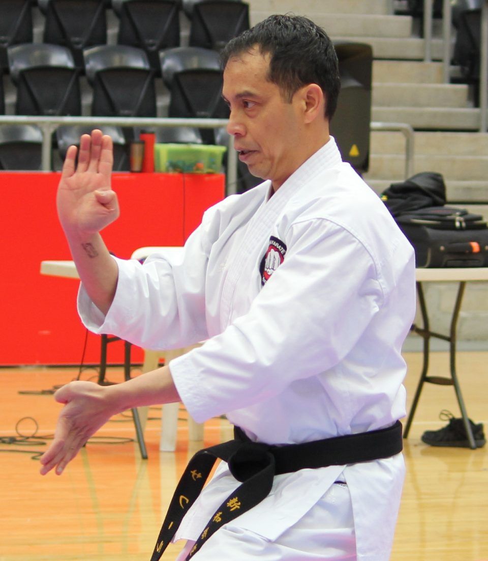 Martial artist in white gi and black belt performing a stance indoors