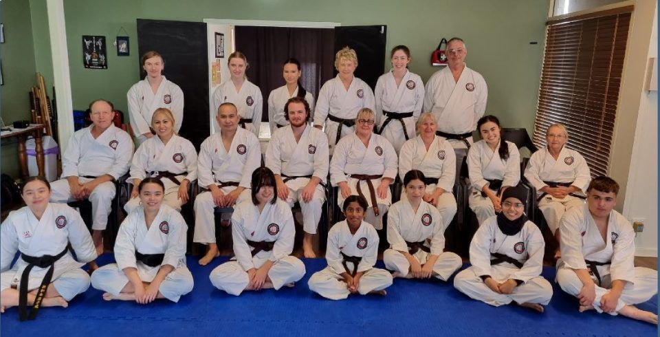Martial arts class group portrait in white uniforms posing on blue mats indoors