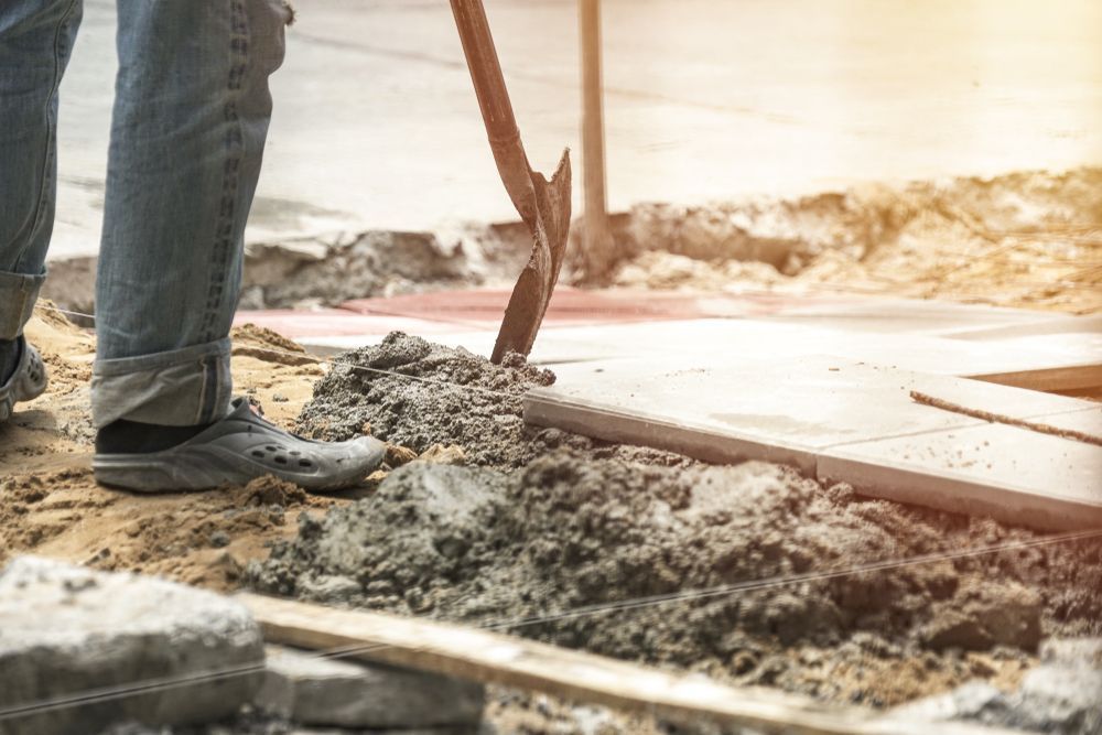 Person in Jeans Digging in Dirt with A Pickaxe at A Construction Site — Wal's Concreting Service Pty Ltd in Lismore, NSW