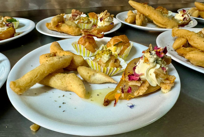 Piatti di stuzzichini dorati e fritti, guarniti con una crema e chicchi di melagrana, su un tavolo