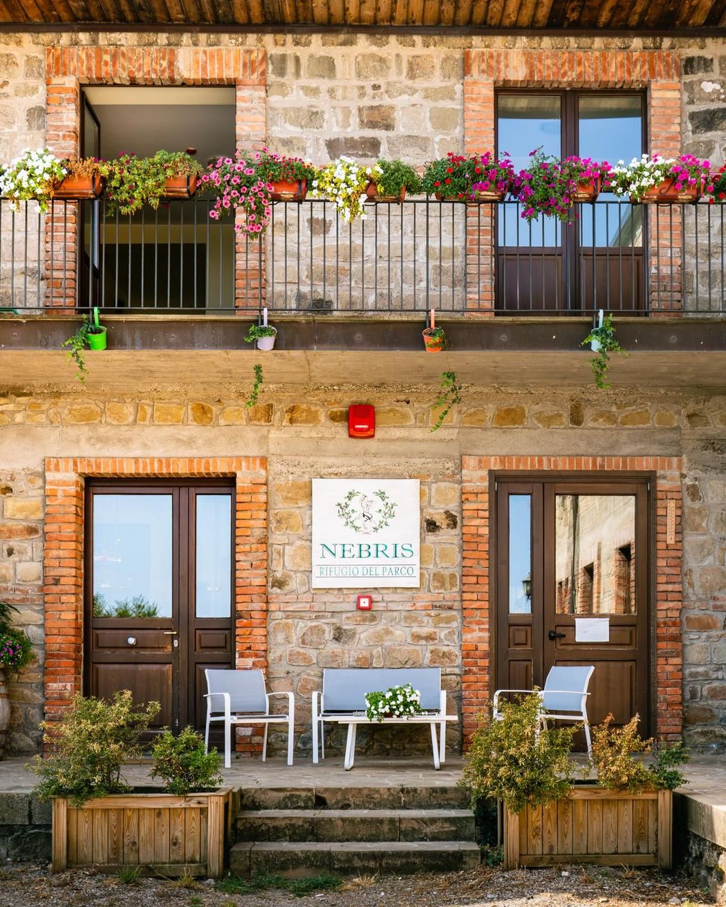 Casa a schiera in pietra, con balconi fioriti, porte in legno e un piccolo patio antistante con sedie e gradini