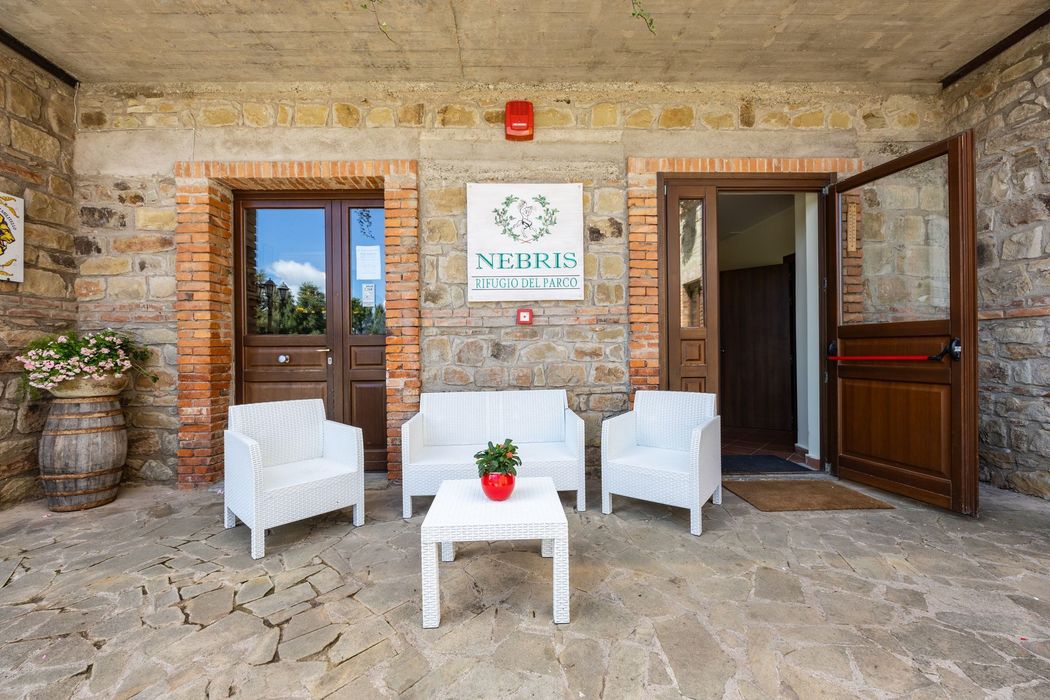Patio in pietra con sedie bianche, tavolino, porte di legno aperte e pareti di mattoni sotto un portico coperto