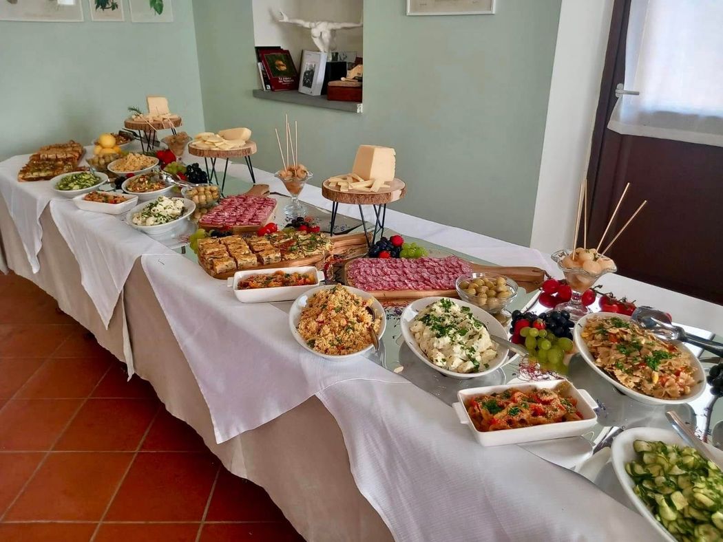Tavolo da buffet con una selezione di piatti, insalate e antipasti, coperto da una tovaglia bianca in una sala da pranzo