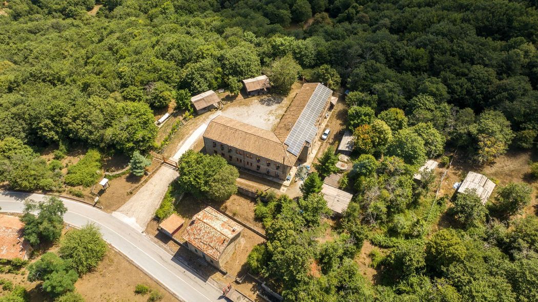 Vista aerea di un grande edificio rustico circondato da una fitta foresta verde e da strade sterrate