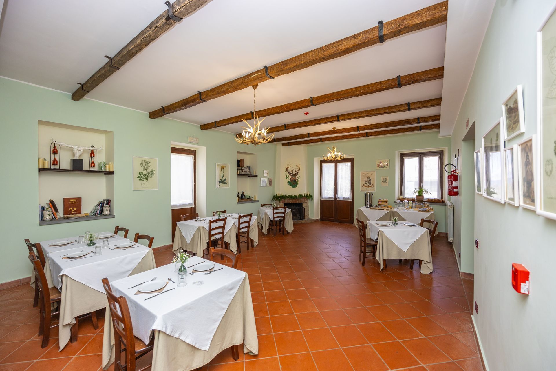 Sala da pranzo con tovaglie bianche, pavimento in cotto e travi di legno a vista in un ristorante rustico