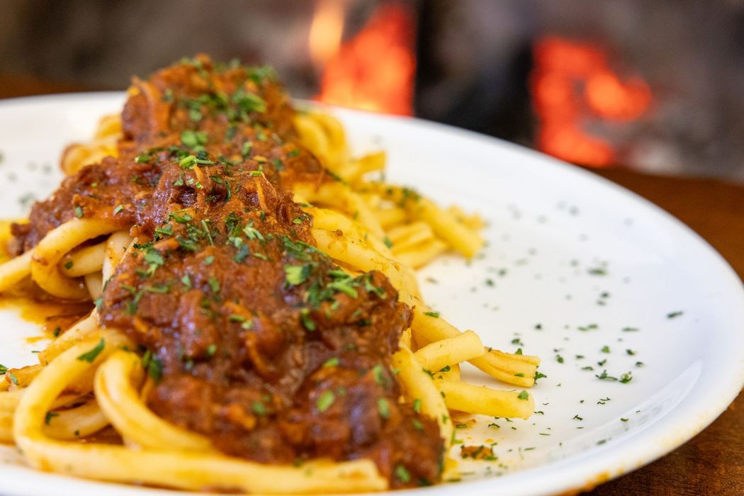 Piatto di pasta al ragù con erbe aromatiche, sullo sfondo sfocato di una griglia a legna