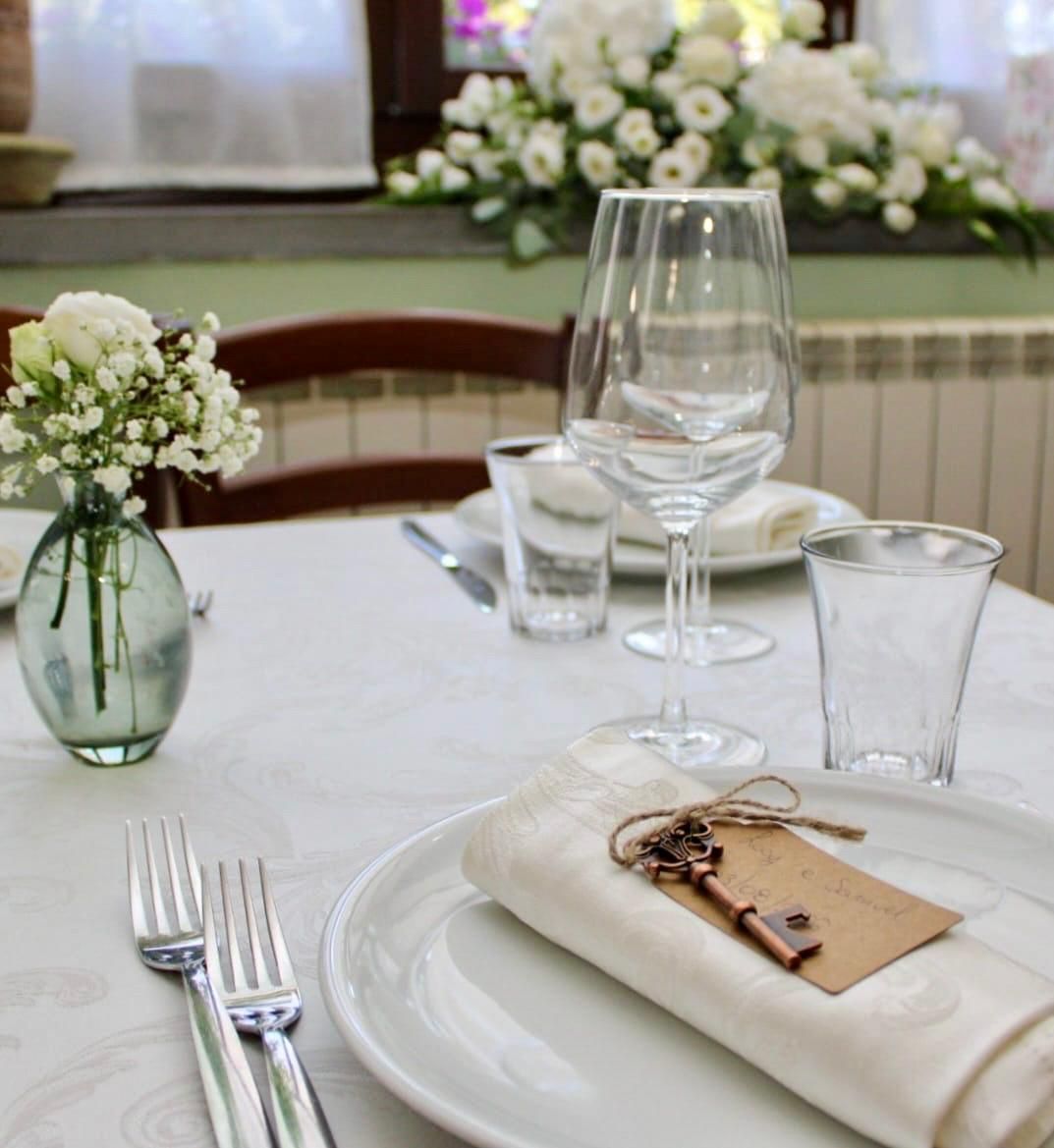 Elegante tavolo da pranzo apparecchiato con tovaglia bianca, bicchieri, tovagliolo e piccoli centrotavola floreali