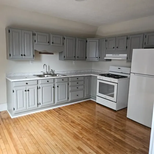 Empty kitchen with gray cabinets, white appliances, and hardwood floors