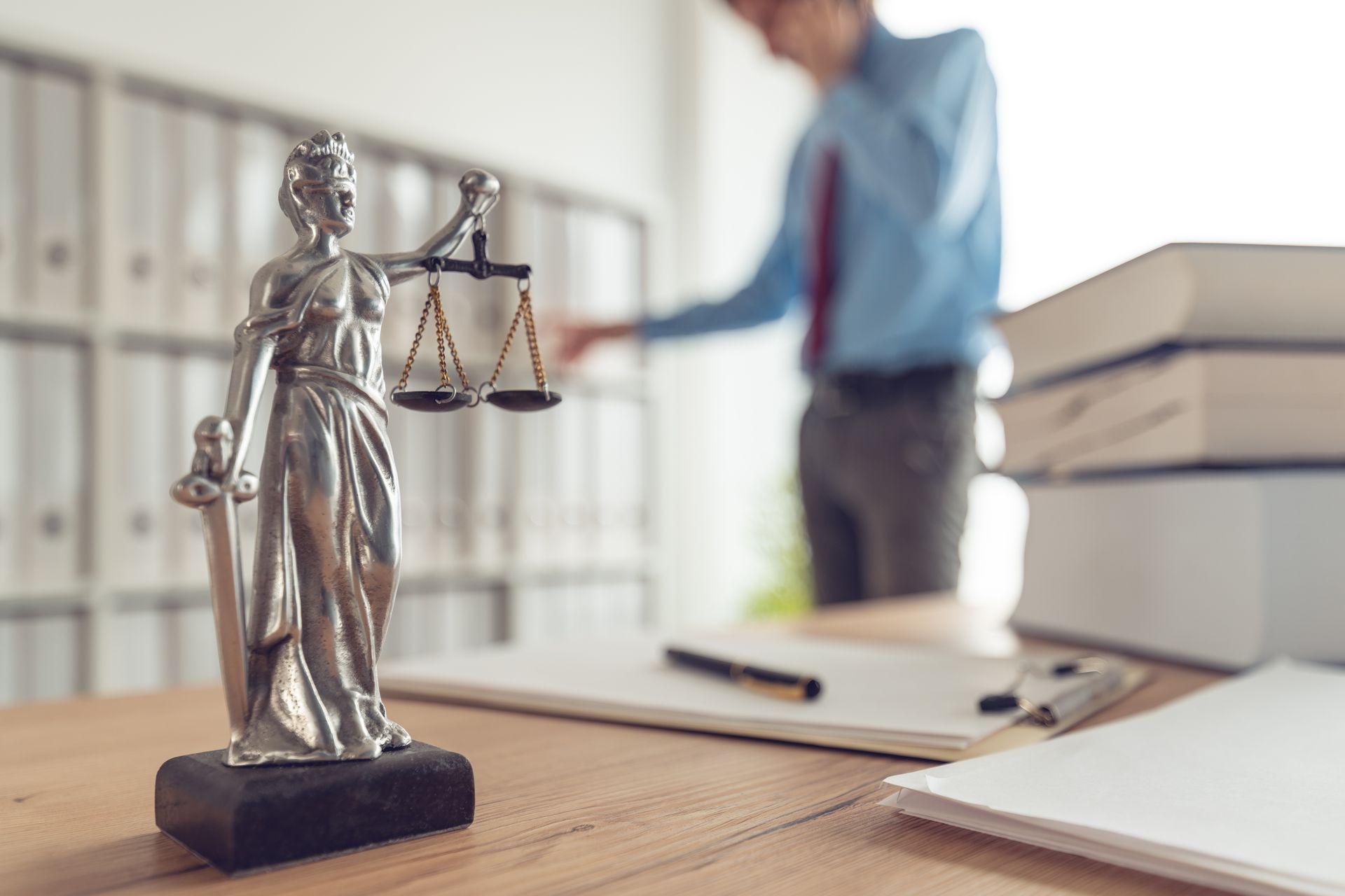 A statue of Lady Justice and books on a table and a lawyer talking on a mobile in the background.