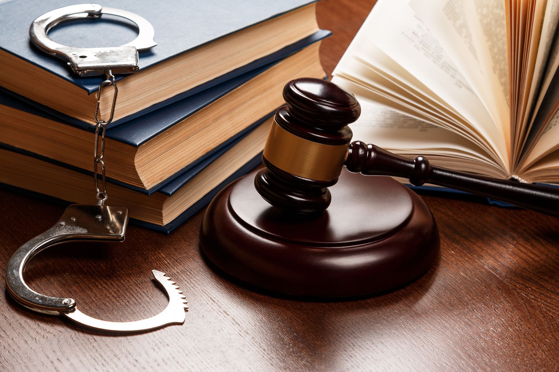 Close-up of wooden gavel, books, and handcuffs, representing criminal law.