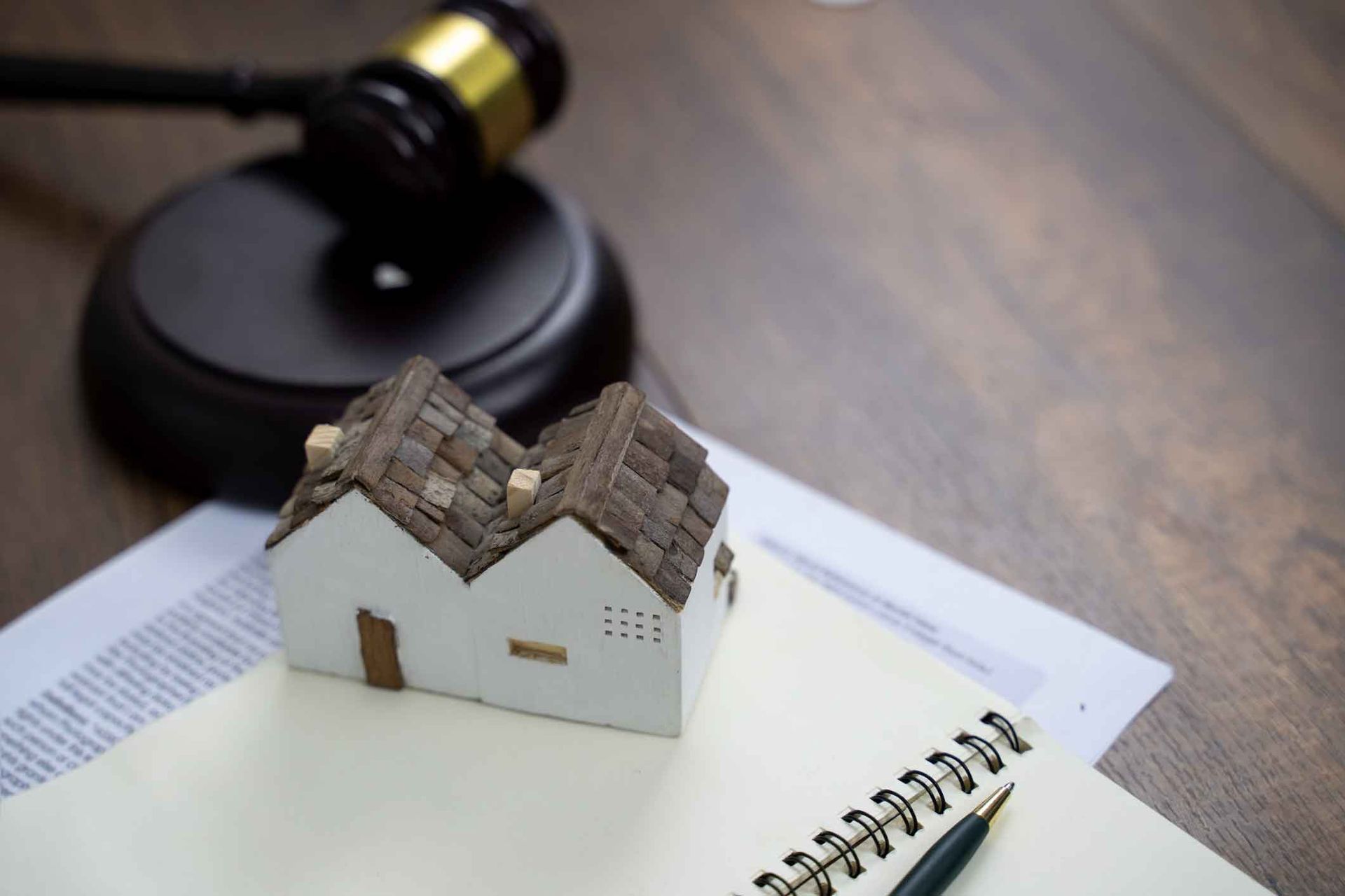 A small model house is sitting on top of a notebook next to a judge 's gavel.