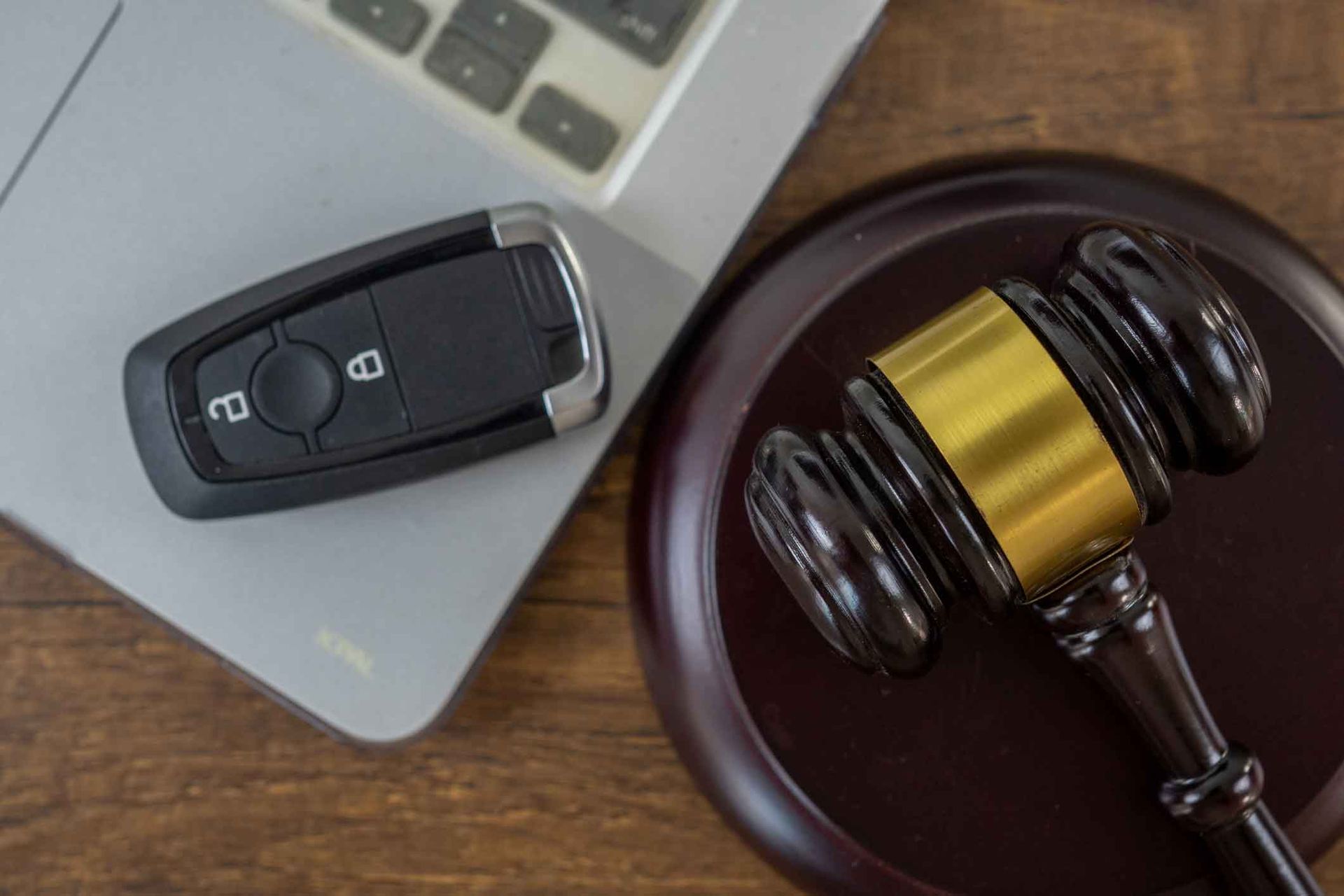 A car key and a judge 's gavel are on a wooden table next to a laptop.