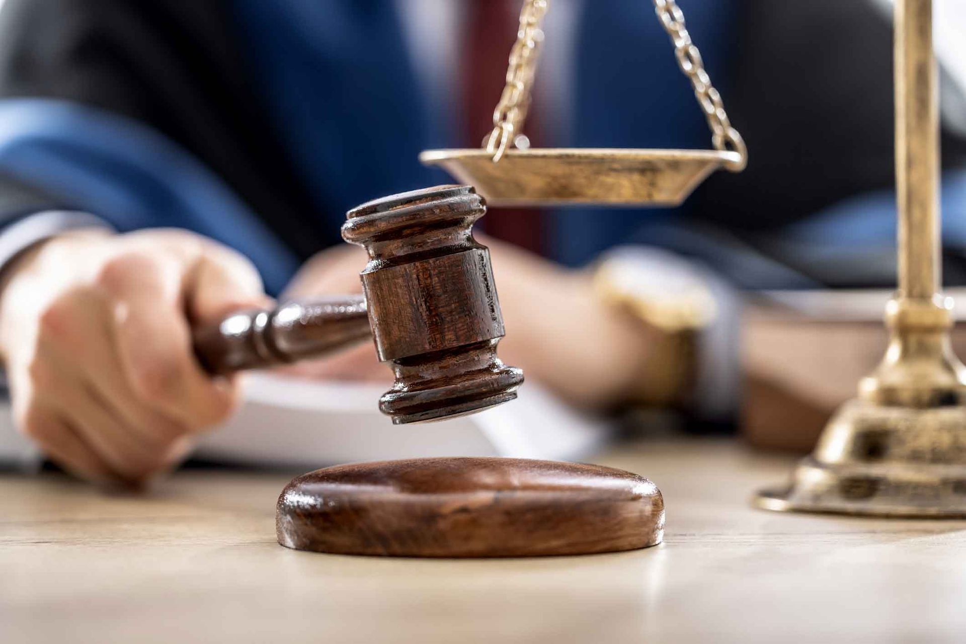 A judge is holding a wooden gavel in front of a scale of justice.