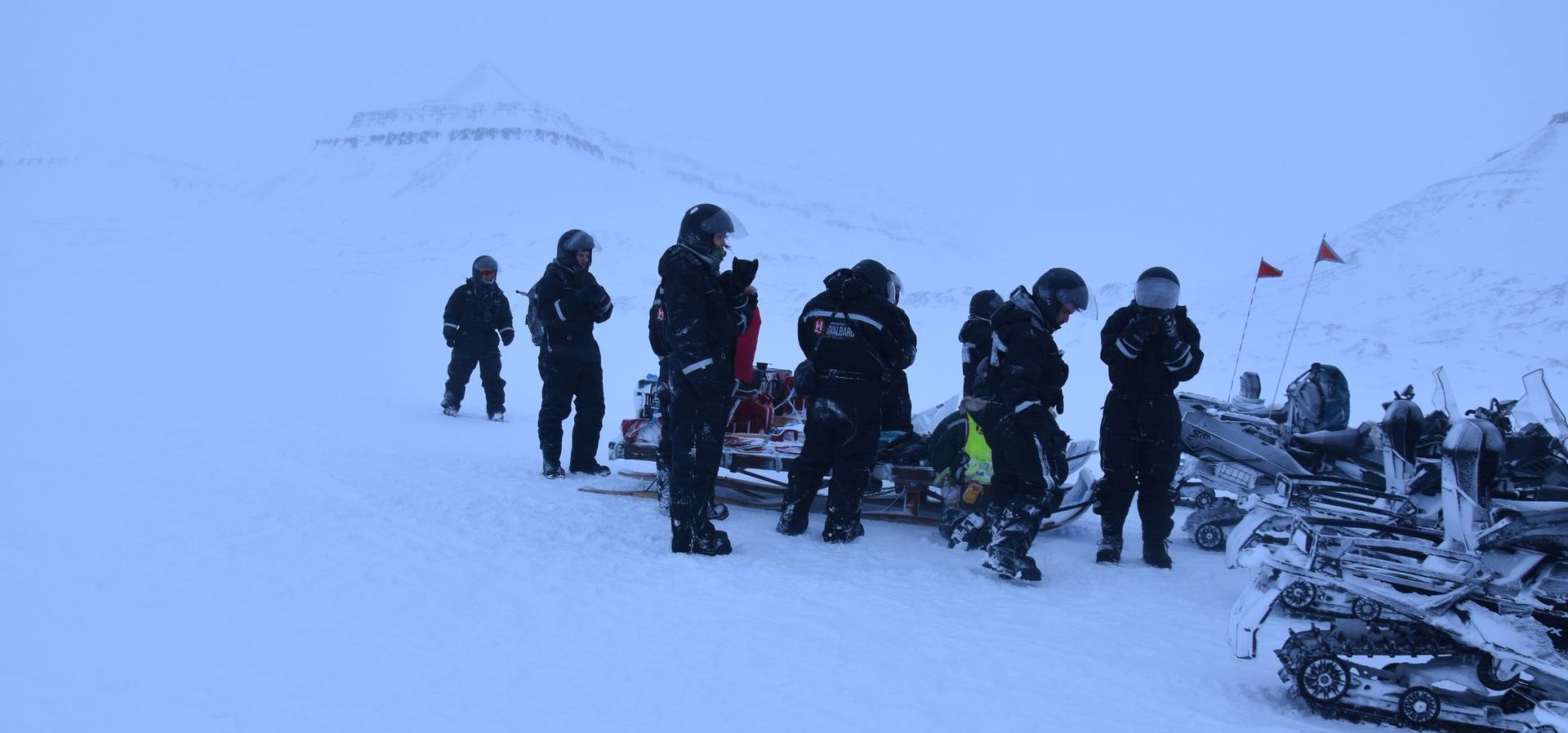 A group of people are standing next to snowmobiles in the snow.