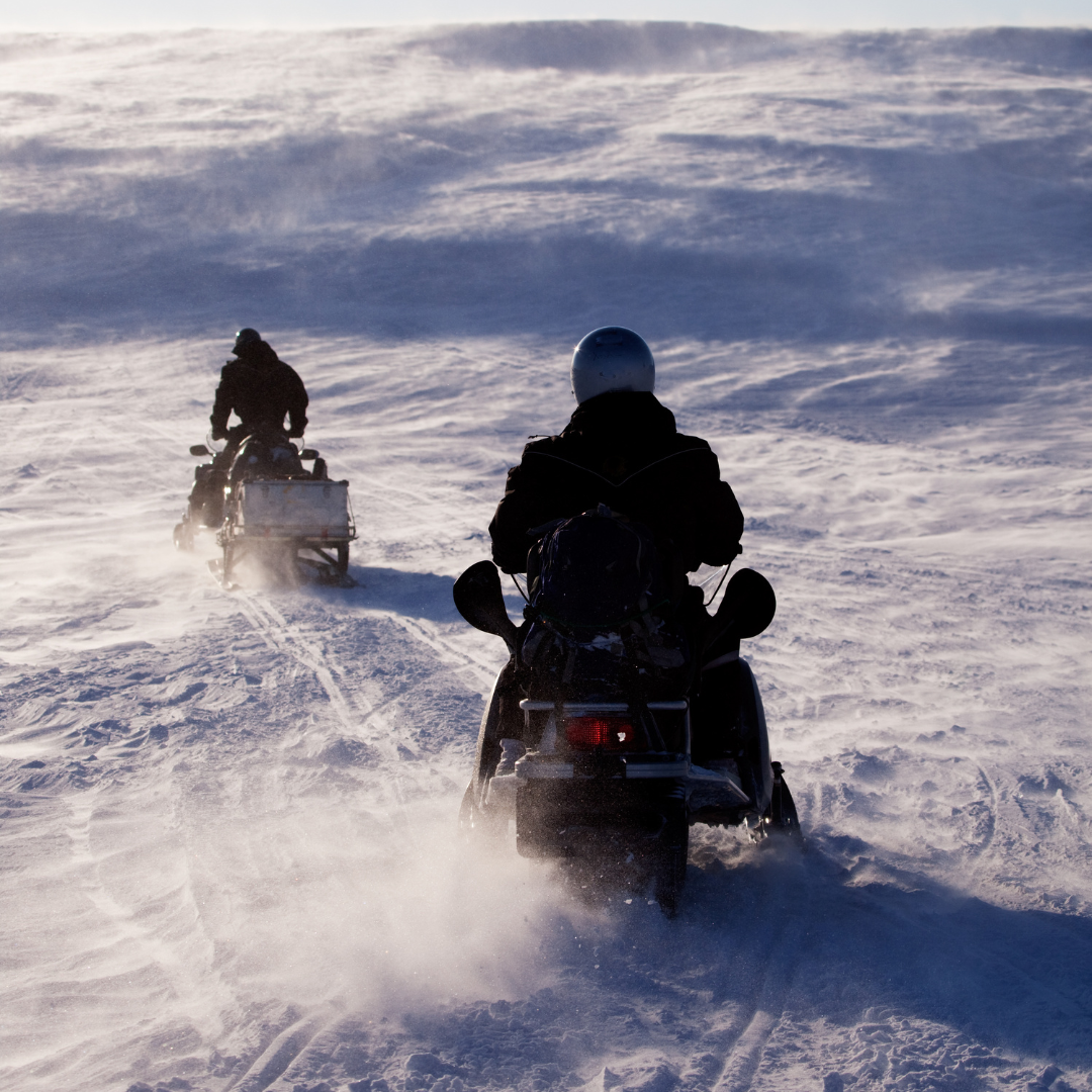 A group of people are riding snowmobiles in the snow.