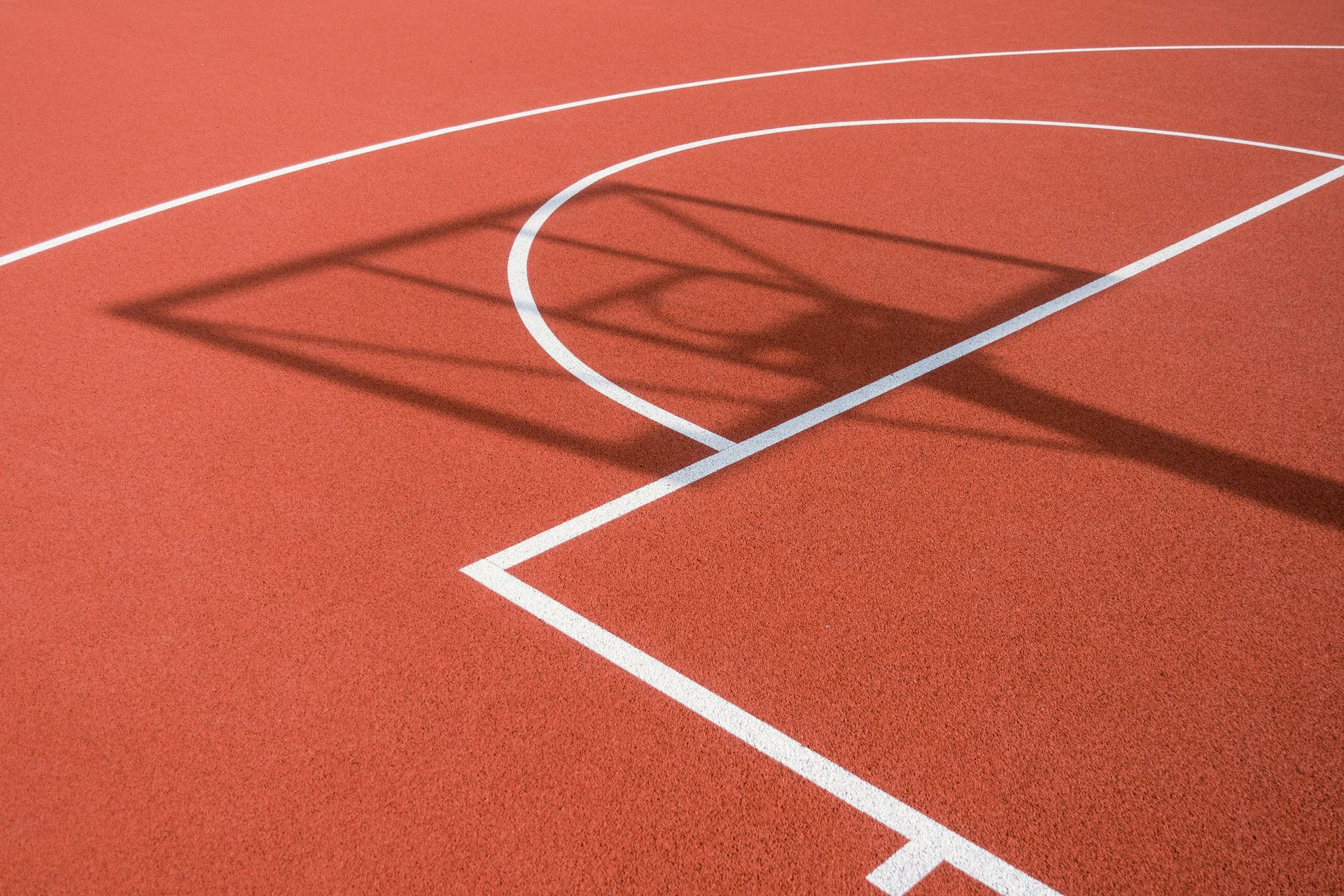 A shadow of a basketball hoop is cast on a red basketball court
