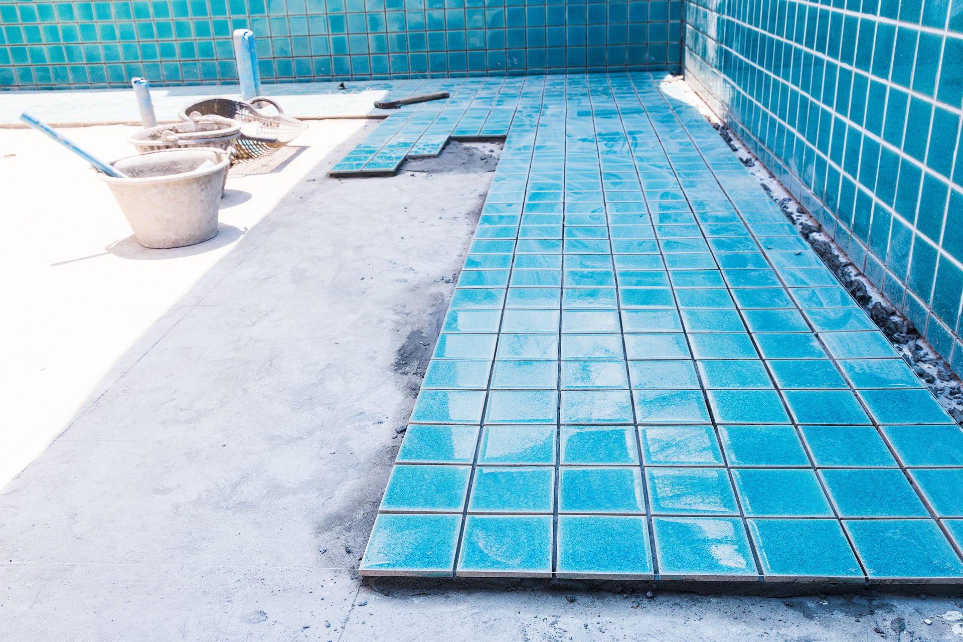 Blue tiles are being installed on the floor of a swimming pool.