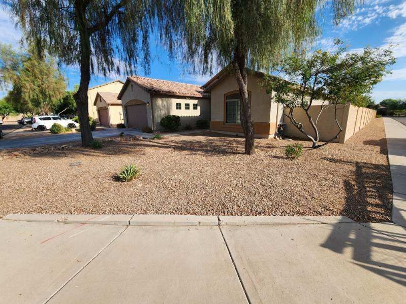 Single-story beige house with a tile roof, desert landscaping, and a sidewalk in front