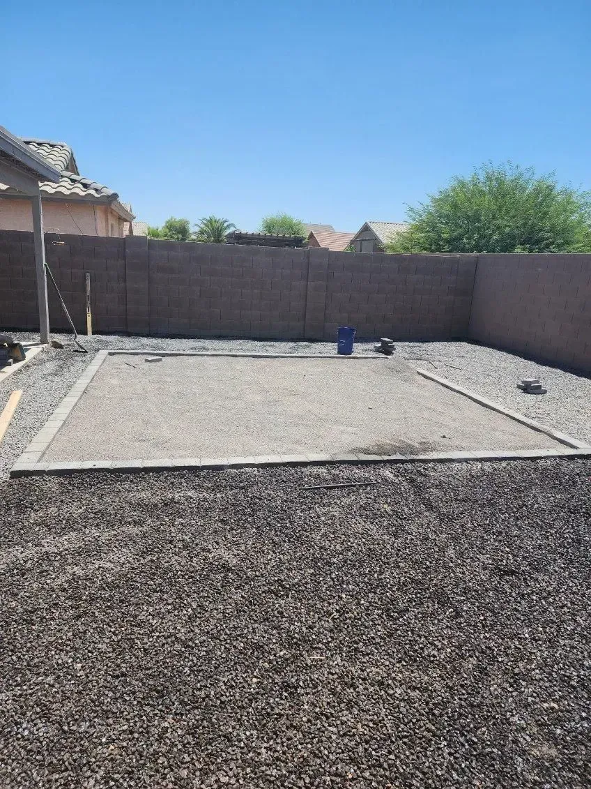 Gravel-filled backyard with raised concrete retaining walls and a blue bucket under a clear sky