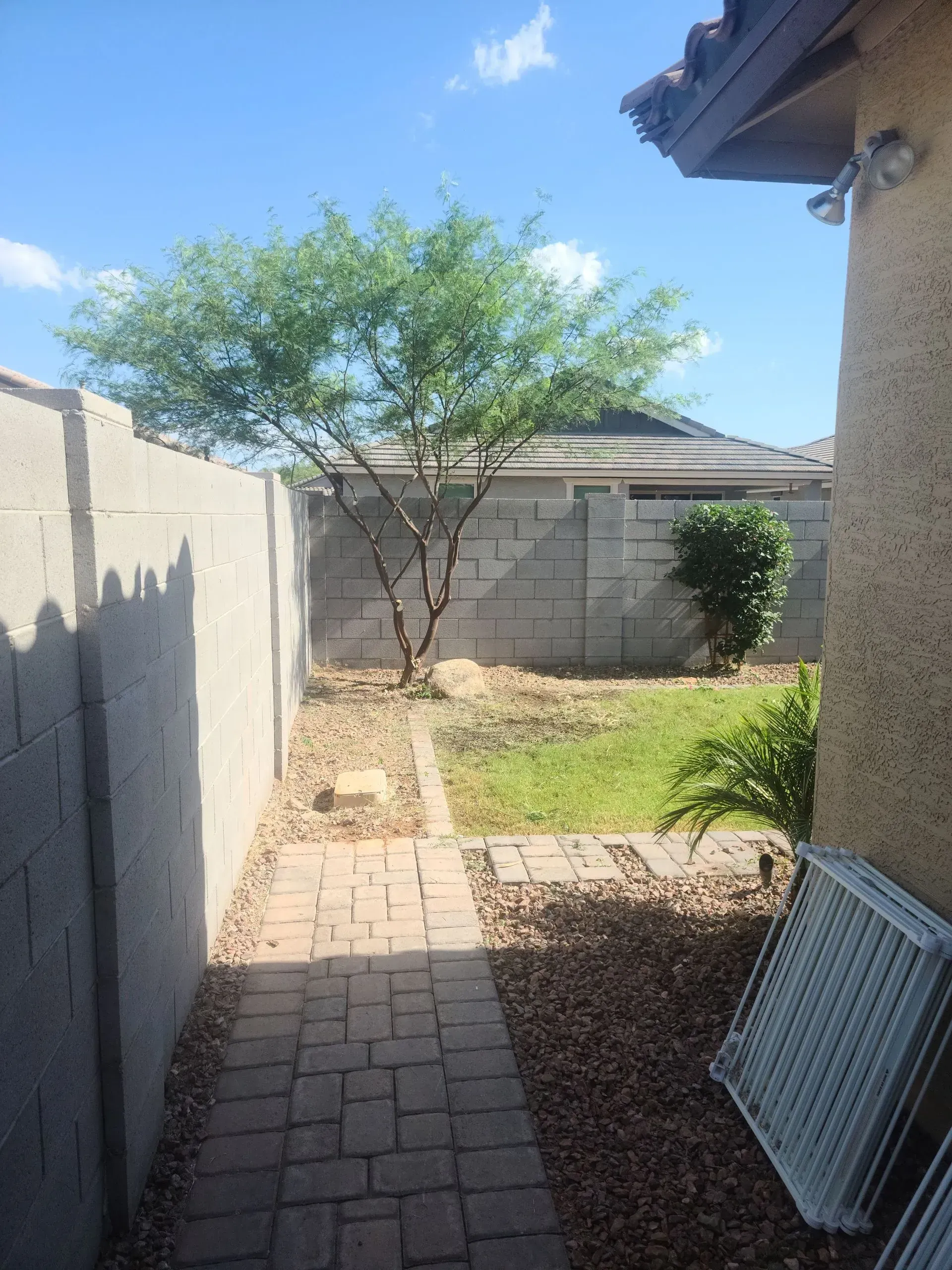 Narrow backyard with pavers, a small tree, grass, cinderblock walls, and a house in the background
