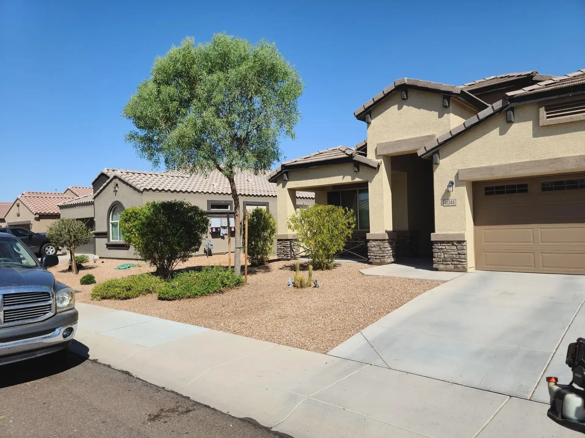 Suburban house with driveway, garage, desert landscaping, and parked cars on a sunny day