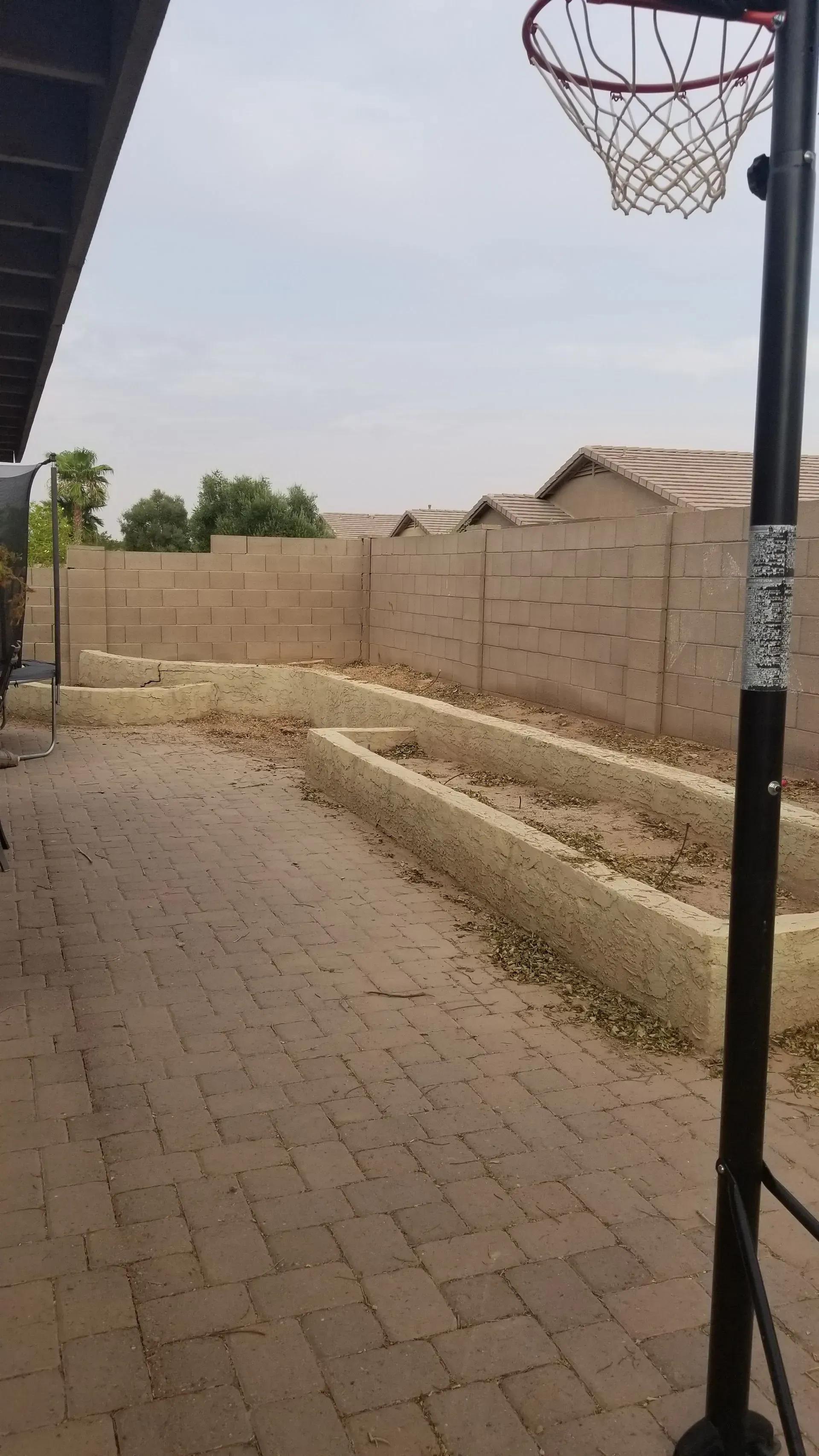 Empty basketball court beside a tan block wall, with a hoop in the foreground.