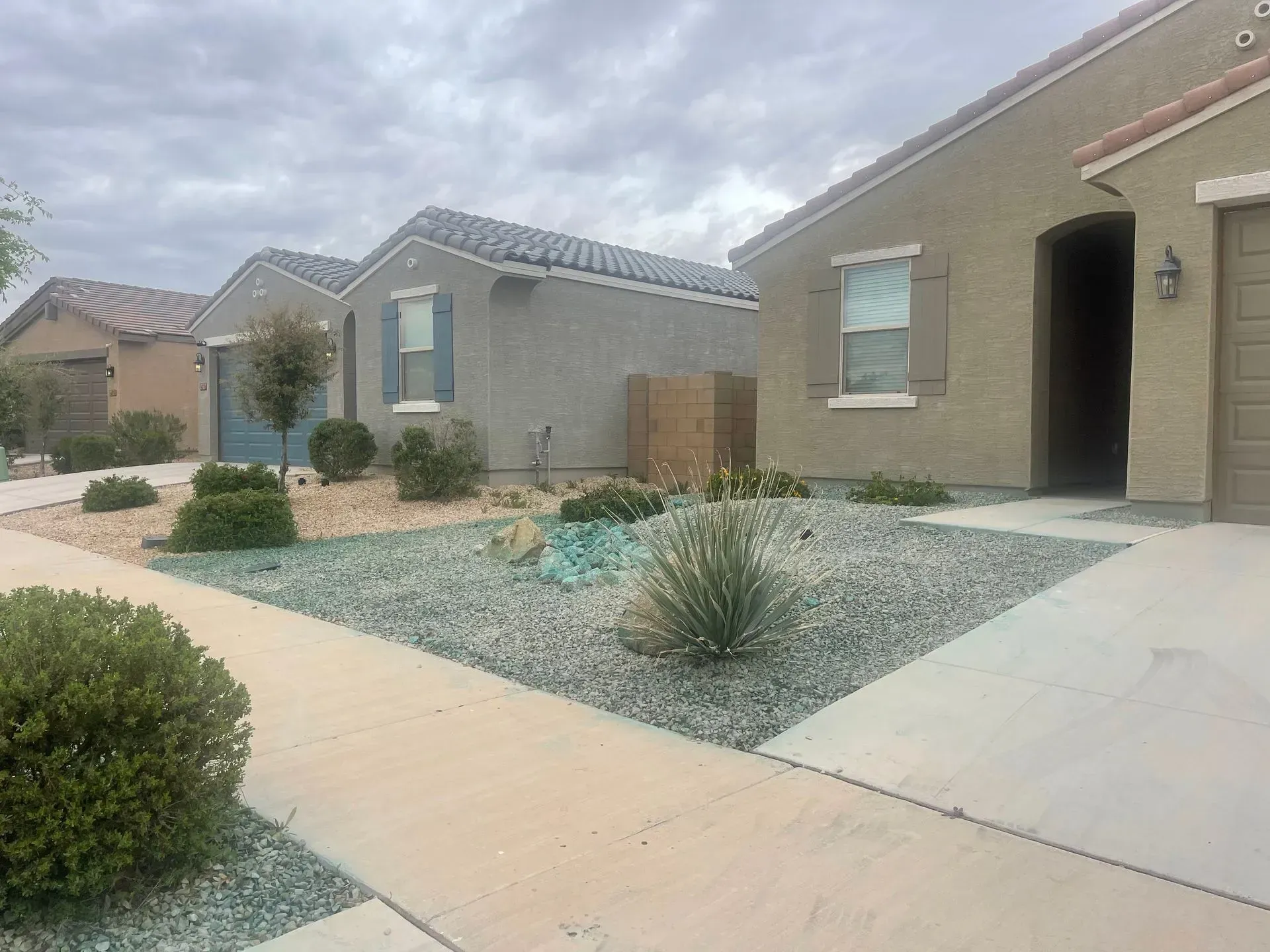 Desert-style suburban homes with gravel landscaping, a concrete walkway, and a front entry under an overcast sky