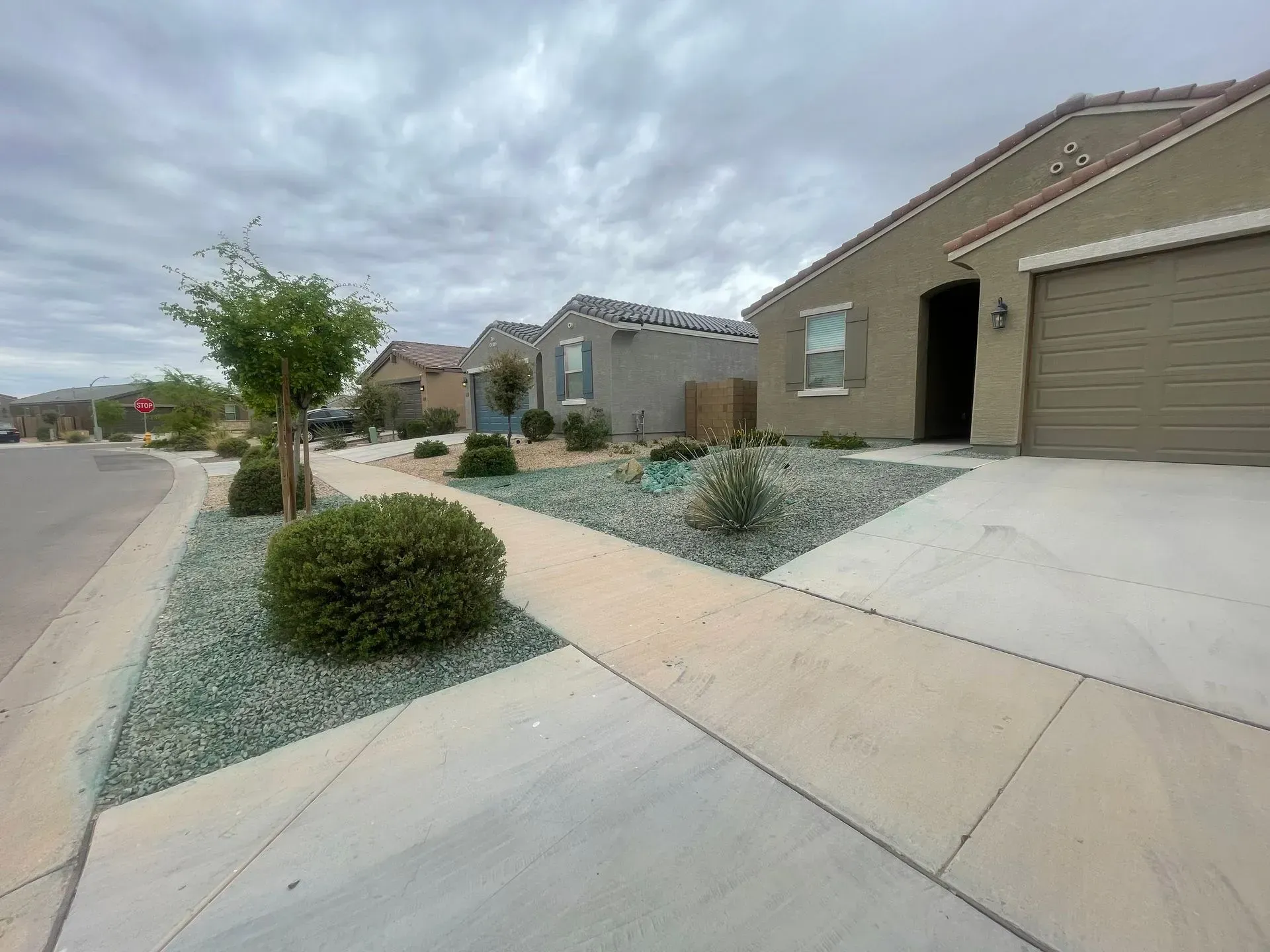Suburban street with modern houses, desert landscaping, and a cloudy sky