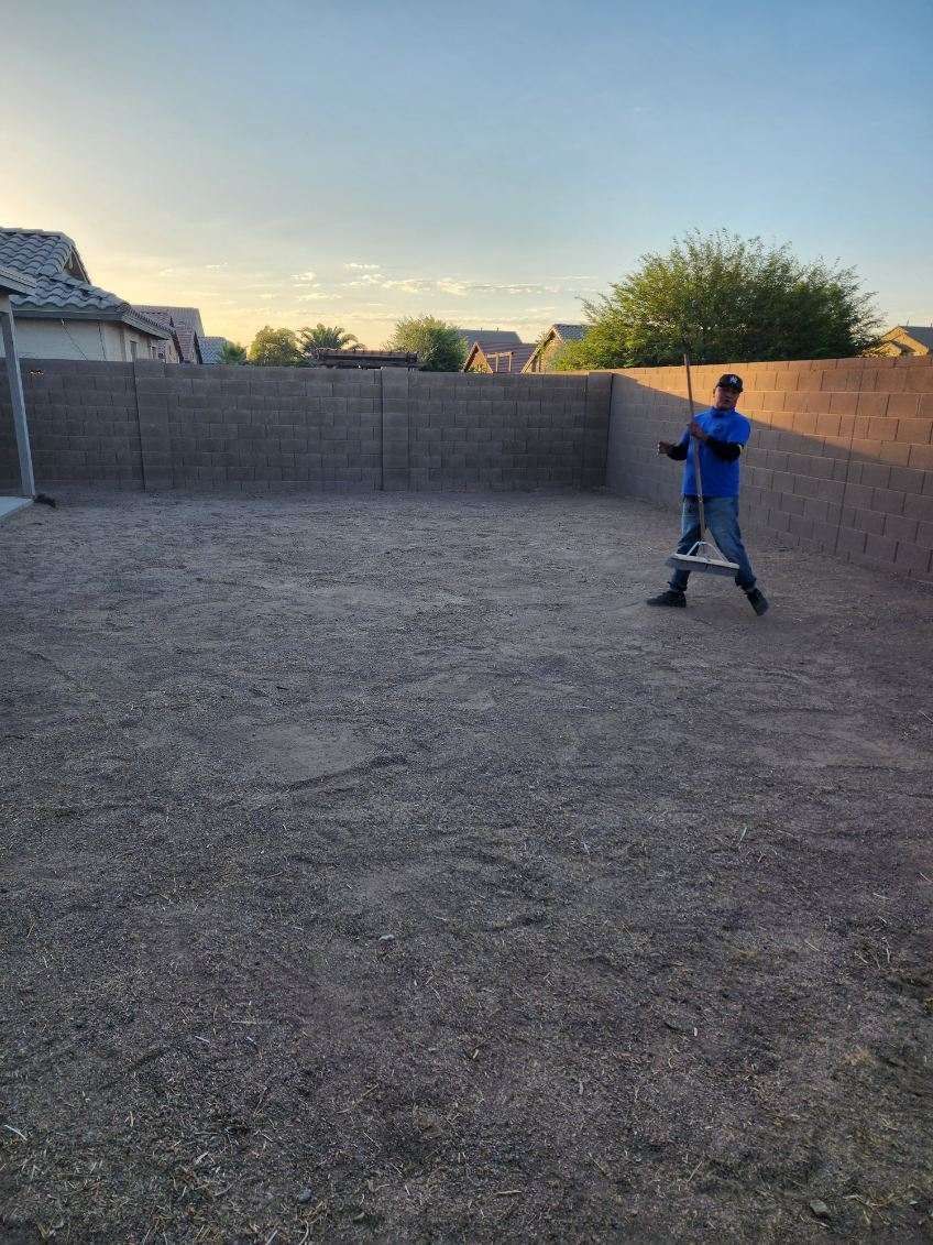 Person in blue shirt standing in a gravel backyard at sunset, near a brick wall.