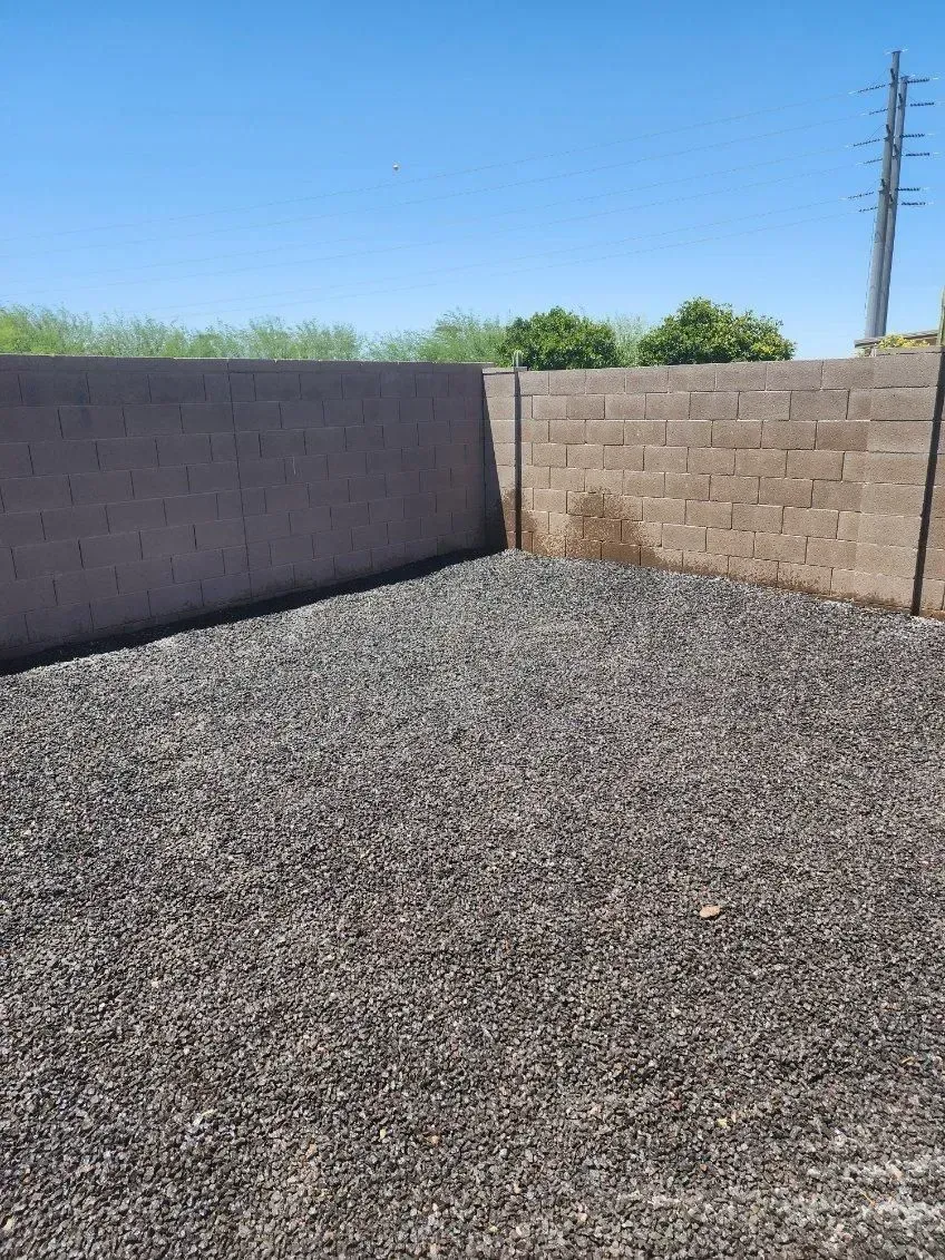 Gravel-covered yard bordered by cinderblock walls under a clear blue sky
