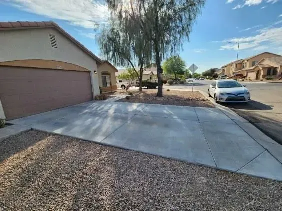 Suburban driveway beside a garage, with a parked white car and desert landscaping under a sunny sky
