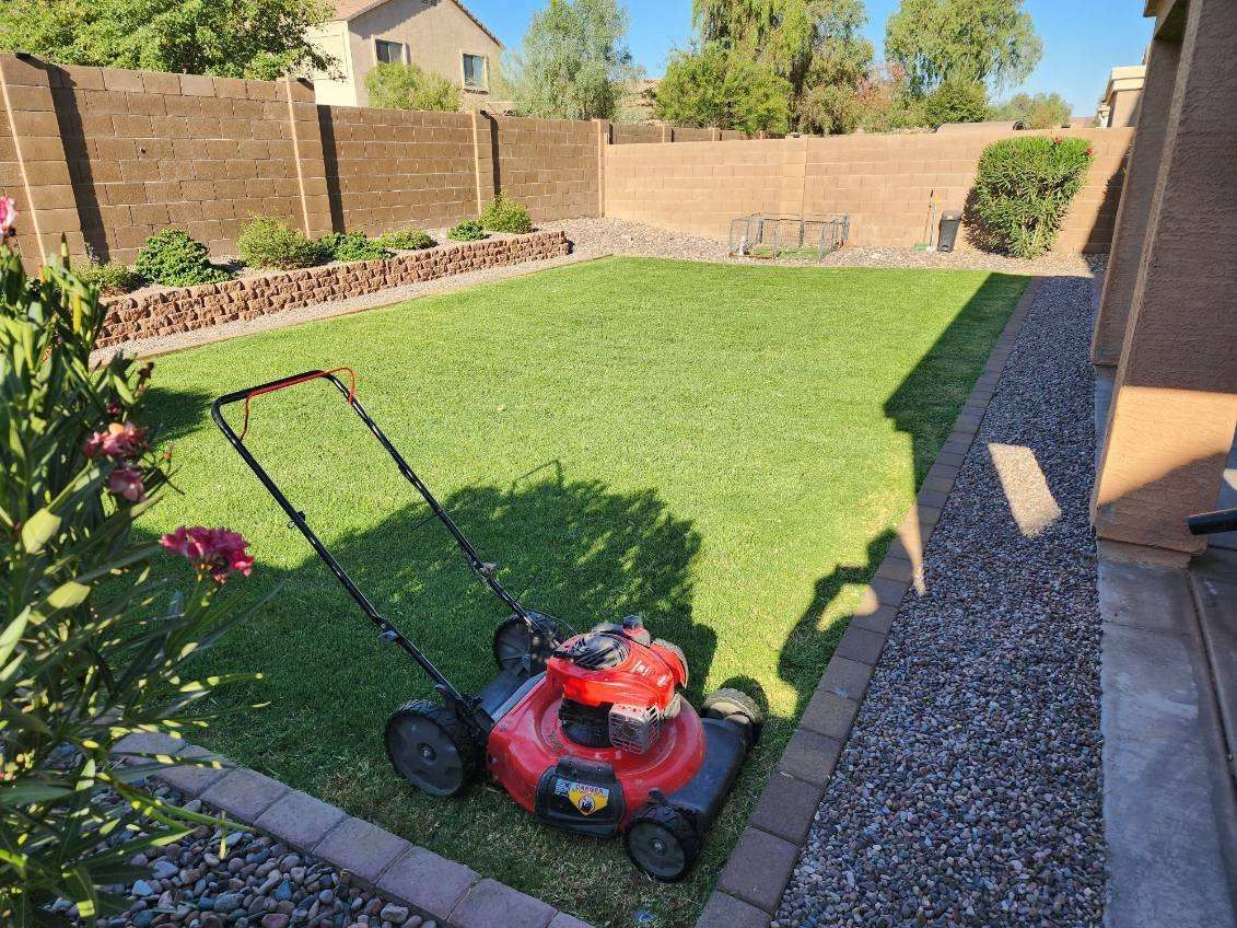 Red lawn mower on a green backyard lawn beside a gravel path and brick wall