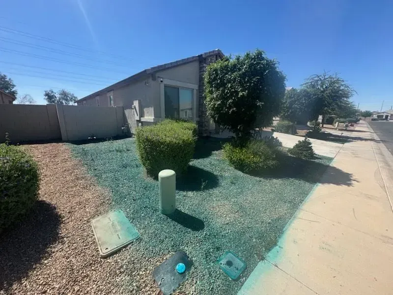 Desert front yard with gravel, shrubs, a house, and a sidewalk along a quiet street.