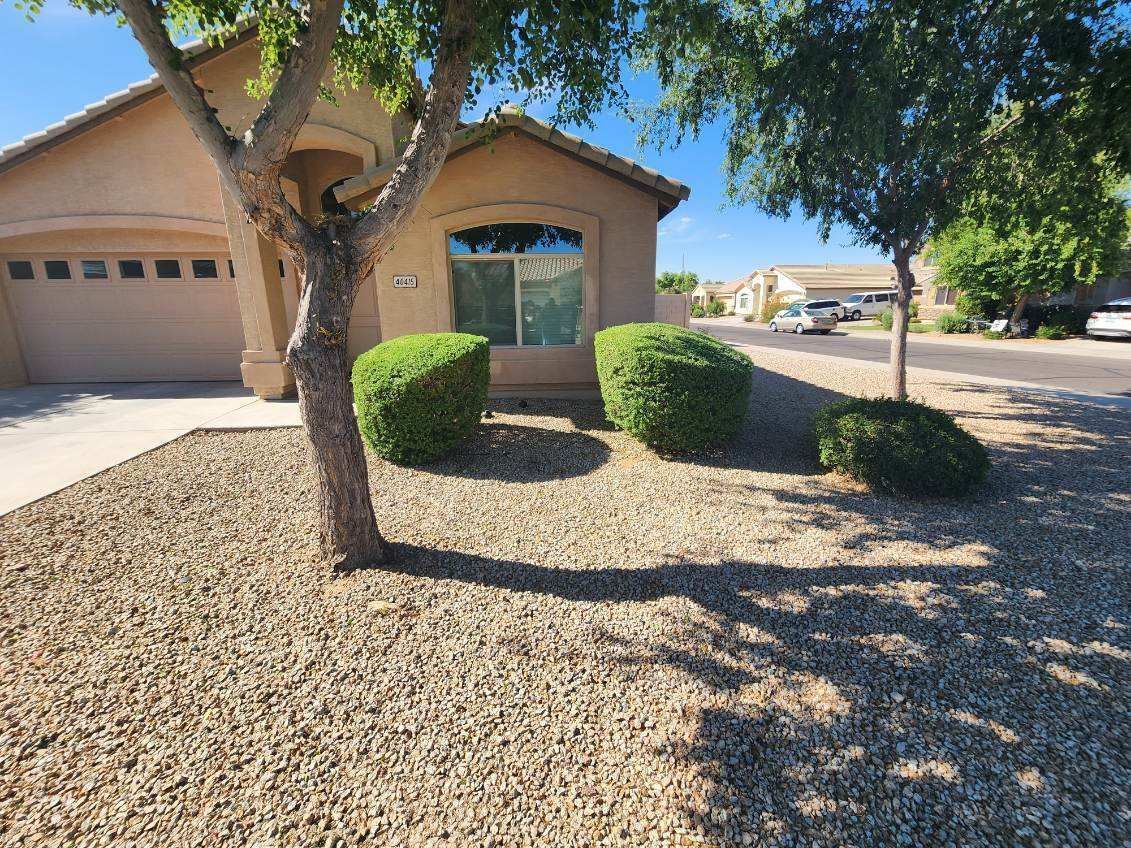 Single-story house with a garage, desert landscaping, and trimmed shrubs under a sunny sky