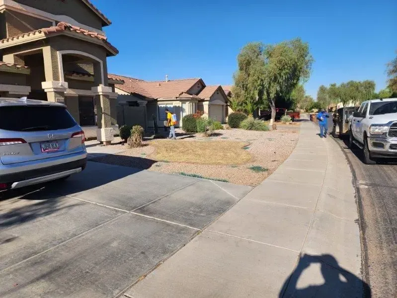Suburban sidewalk beside stucco houses, parked cars, and a sunny desert street under a clear blue sky