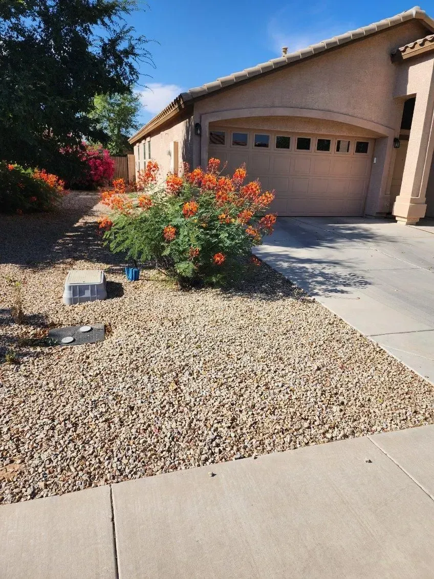 Front yard with gravel landscaping, orange flowering bushes, and a beige house with a garage.