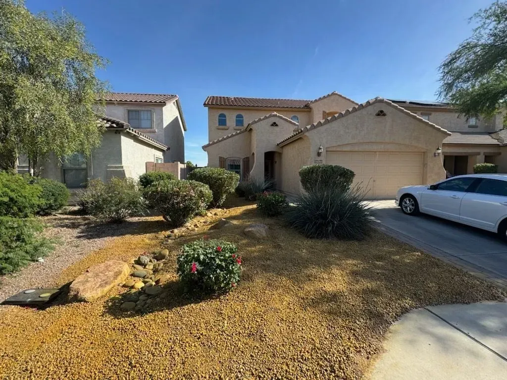 Suburban house with tan stucco, dry front yard landscaping, and a car parked in the driveway