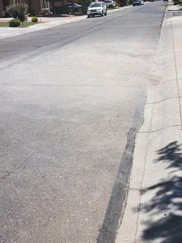 Quiet residential street with a cracked asphalt road and a parked car in the distance