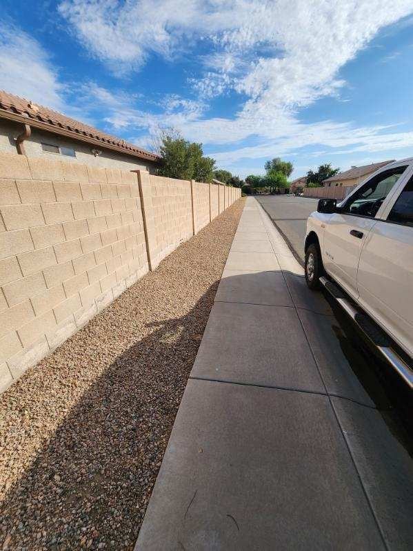 Sidewalk beside a tan block wall under a blue sky, with a parked white SUV on the right.