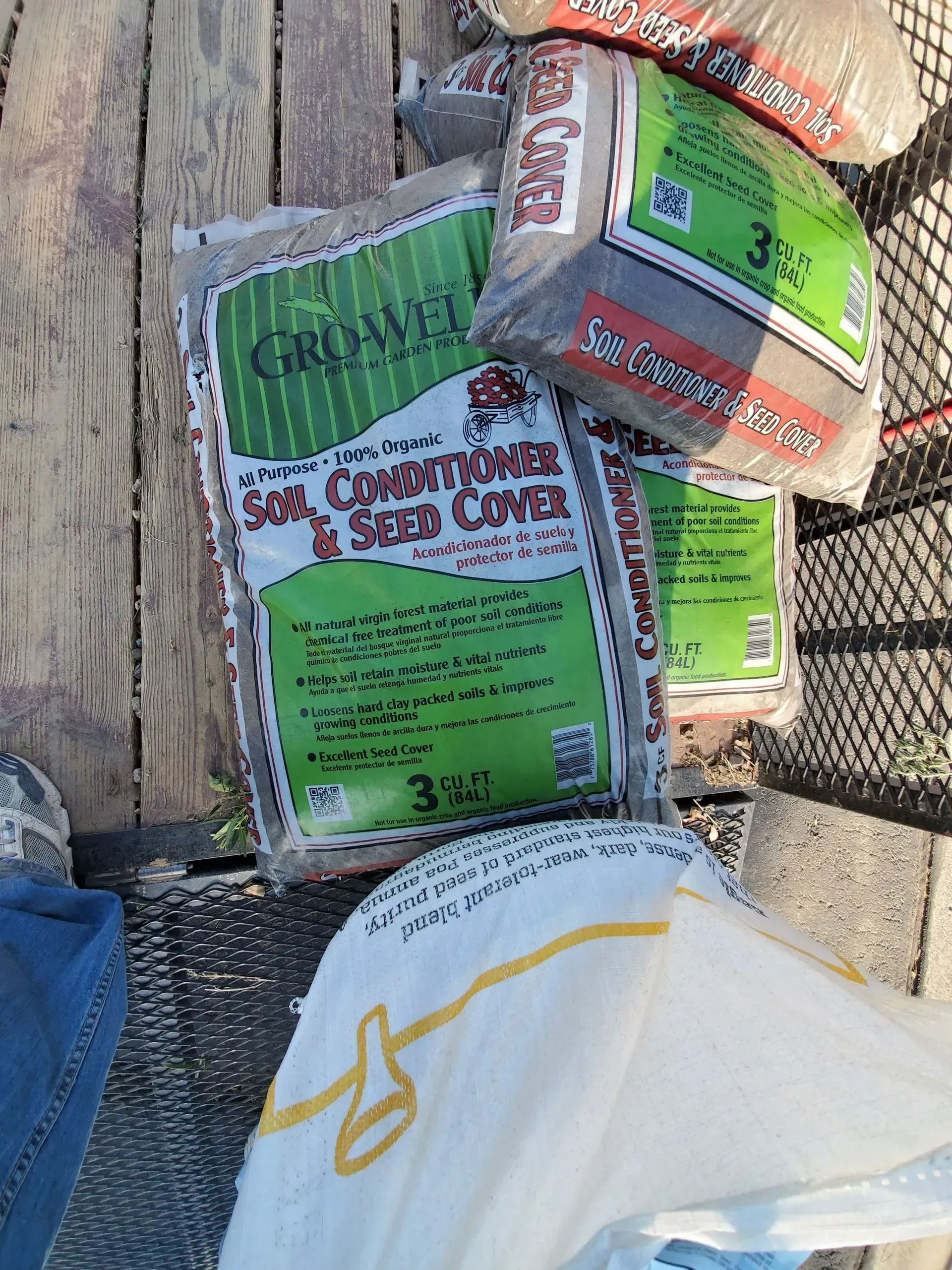 Stacked green and orange garden seed packets on weathered wood, with a white bag in the foreground
