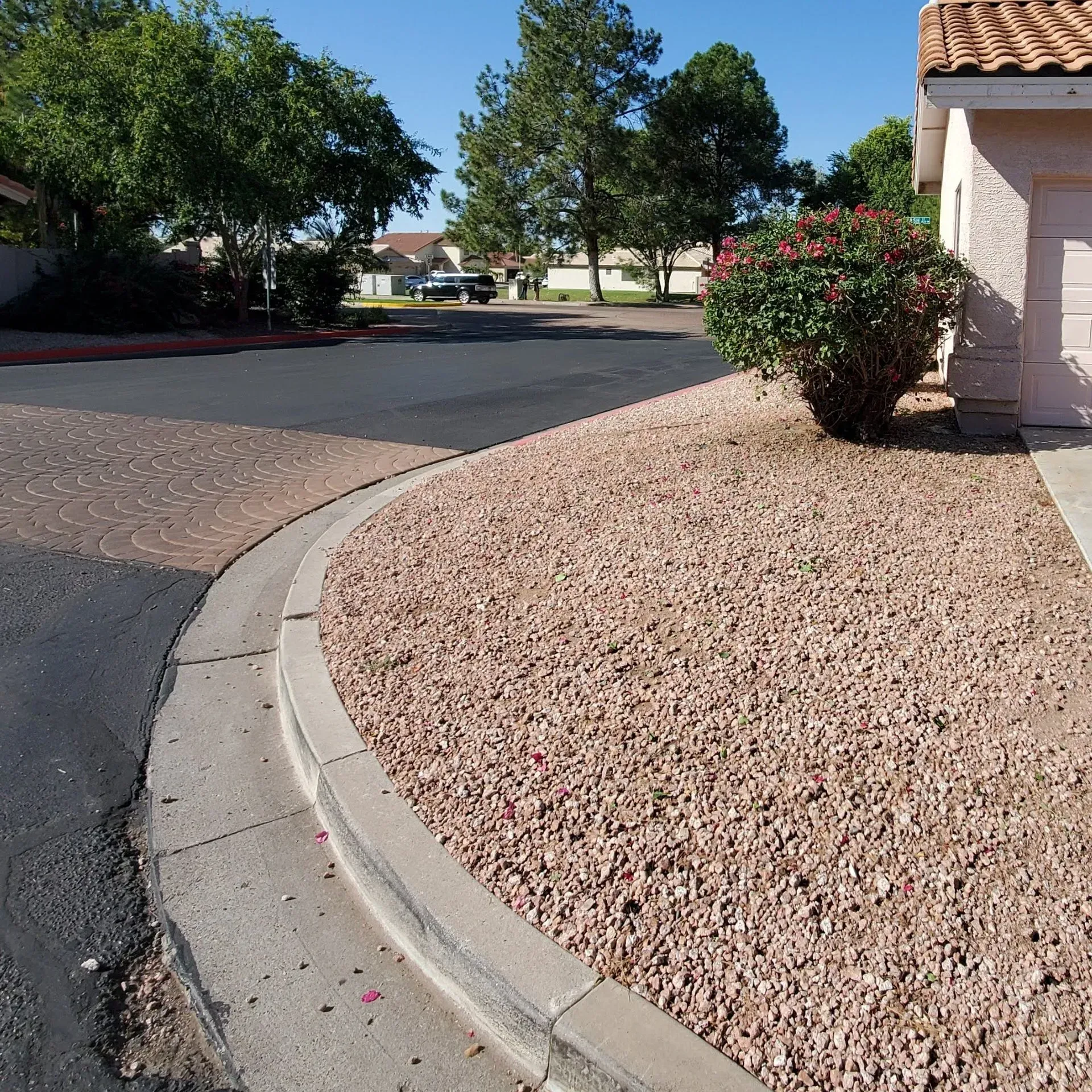 Curved curb beside a gravel yard and house, with trees lining a quiet residential street.