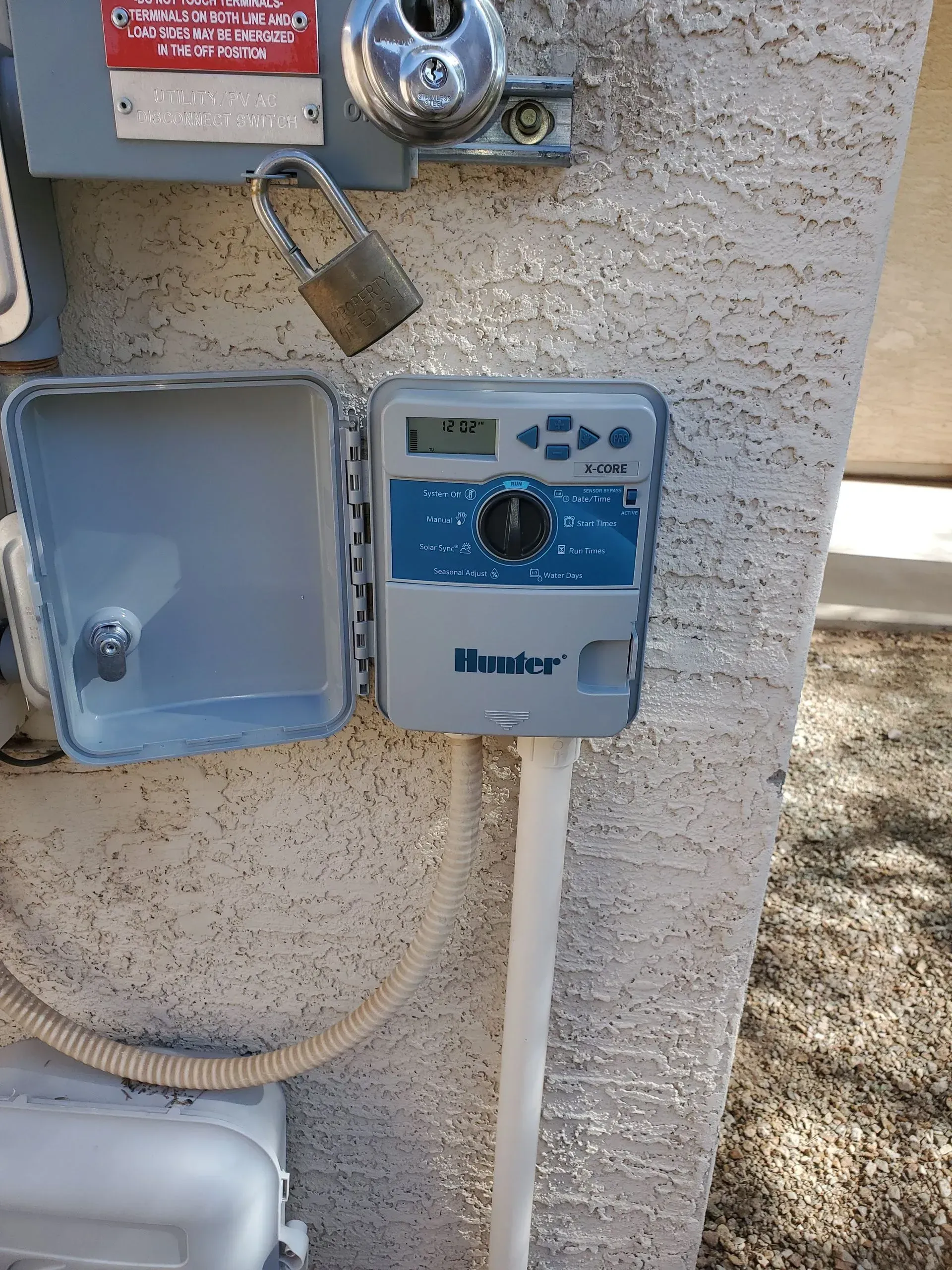 Open electrical control box with a blue irrigation timer mounted on a stucco wall.