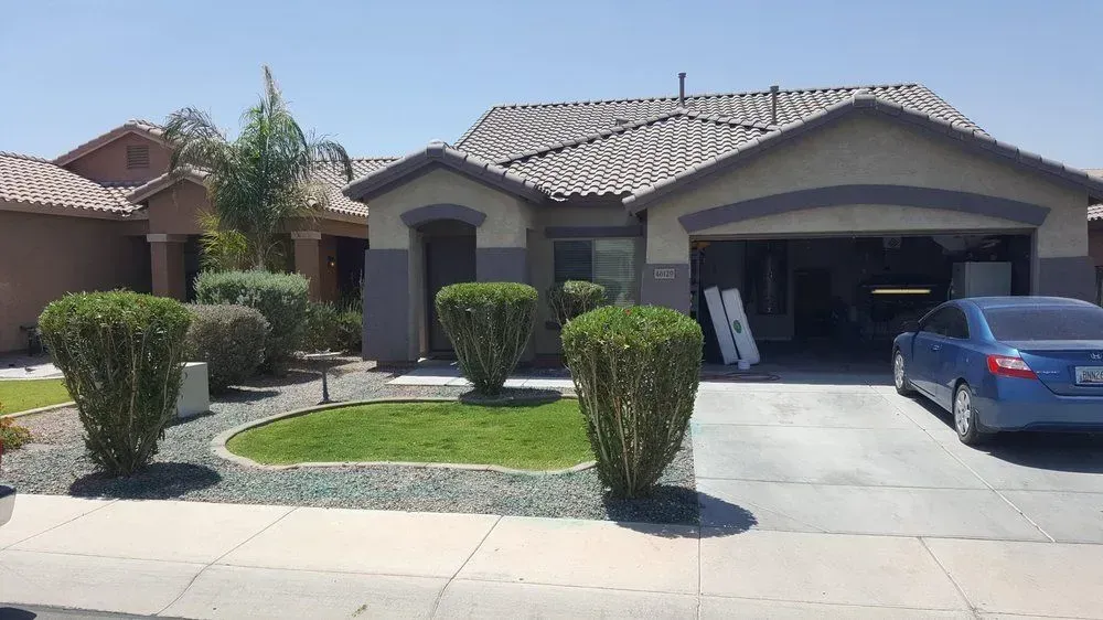 Suburban house with a two-car garage, trimmed shrubs, and a blue car parked in the driveway.