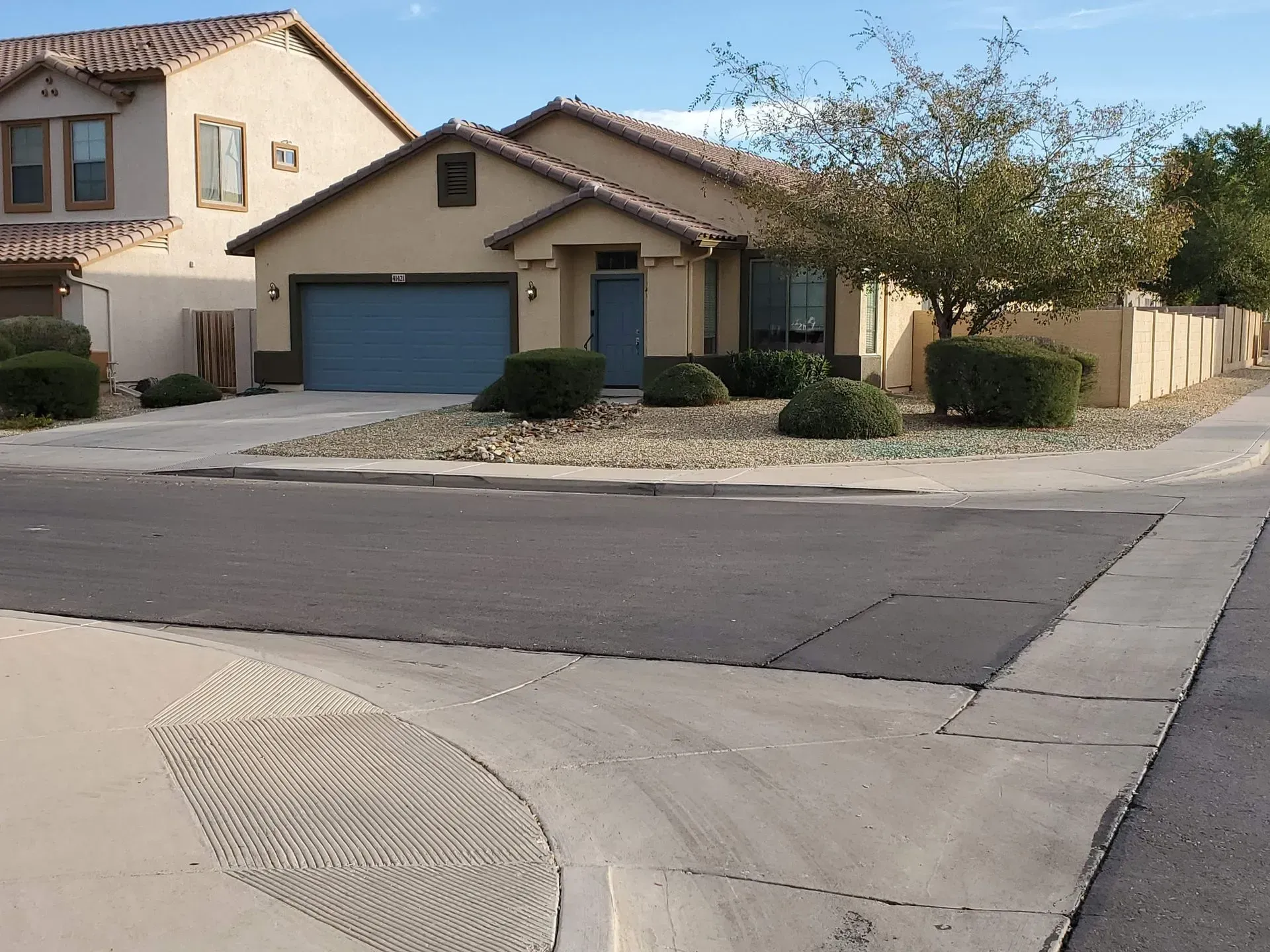 Suburban street corner with beige houses, a blue garage, and a sidewalk curb ramp