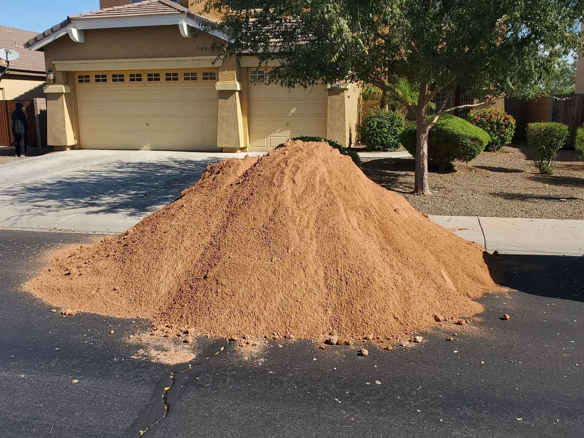 Large mound of tan dirt piled on a residential driveway in front of a house